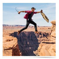 Man taking a leap over a gap in a canyon.